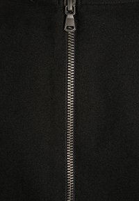 Zwart stoffen kledingstuk met een metalen rits met zilveren tanden aan de voorkant, wat detail toevoegt aan de gladde textuur.