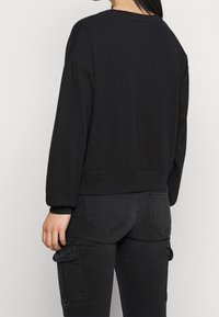 Sudadera negra de manga larga, con hombros caídos y un dobladillo acanalado. Combinada con pantalones cargo negros ajustados que cuentan con bolsillos laterales.