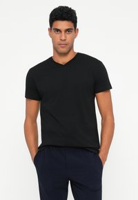 Black short-sleeve V-neck t-shirt made of cotton, featuring a plain design and a relaxed fit, paired with dark navy pants.