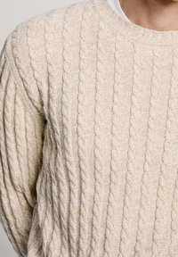 Beige Kabelstrickpullover mit gerippter Textur und rundem Ausschnitt, aus einem weichen, leichten Stoff.
