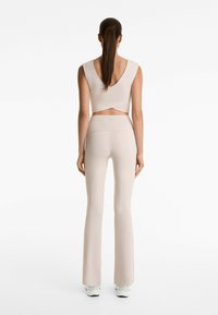 Beige atletisk crop top med djup V-rygg, ihopparad med utsvängda leggings av samma material och färg, som har en slät och figurnära design.