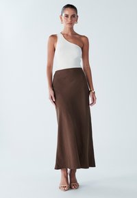 Asymmetriskt vitt ribbat linne parat med en lång, svepande brun kjol. Slät textur, minimalistisk design och sandaletter i nude kompletterar looken.