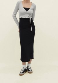 Cardigan accorciato grigio a coste con dettaglio di legatura, indossato sopra un vestito fitted nero. Sneakers nere e grigie con dettagli bianchi e calze.