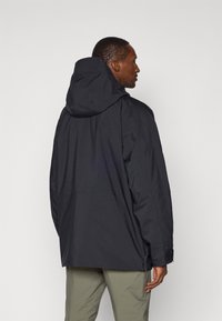 Black waterproof jacket with a hood, featuring a loose fit, minimalistic design, and zipper details at the cuffs and hem.