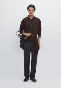 Donkere bordeaux lange mouwen polo, losse marine blauwe broek, bruine suède schoenen en een bruine leren schoudertas met een band.