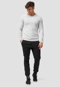 Lichtgrijs lang sleevenshirt met een ronde halslijn, gecombineerd met zwarte taps toelopende broek en zwarte sportschoenen. Eenvoudig ontwerp en aansluitende pasvorm.