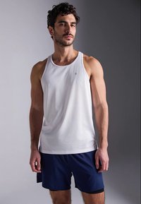 Camisola sem mangas branca feita de tecido suave, combinada com calções azul-marinho. Design simples com decote redondo e mínima marcação.