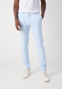 Világoskék, slim fit chinos, elülső gombos záródással, oldalsó zsebekkel és sima, könnyű anyagból. Fehér sportcipővel párosítva.
