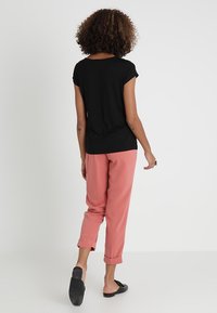 Top negro de manga corta con un corte holgado, combinado con pantalones rosas con puños. La modelo lleva zapatos negros sin cordones. Diseño sencillo con textura suave.