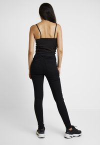 Jeans ajustados negros de cintura alta, tejido texturizado y bolsillos traseros clásicos. Combinados con un top negro de tirantes finos y zapatillas negras.