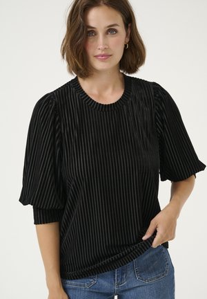 Top din catifea neagră cu pliuri verticale, decolteu rotund și mâneci scurte tip puff. Asortat cu blugi din denim albastru.