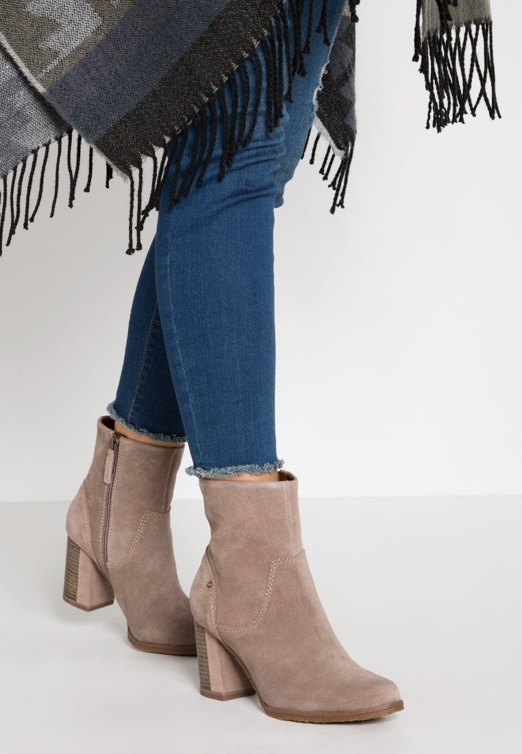 Botas de tobillo de ante topo con tacón cuadrado, cremallera lateral y costuras decorativas; llevadas con jeans de dobladillo deshilachado.