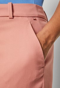 Lichtroze broeken met een getextureerde stof, voorzien van een zijzak en een klein label nabij de tailleband. Gladde afwerking en op maat gemaakte pasvorm.