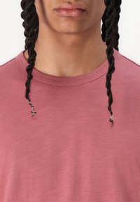 Roze T-shirt met een ronde hals, met subtiele textuur en zichtbare vlechten nabij de halslijn. Geen patronen of hardware aanwezig.