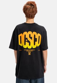 Zwarte t-shirt met gedurfde geel-oranje gradient tekst op de achterkant. Ruime pasvorm met korte mouwen en een standaard ronde hals.