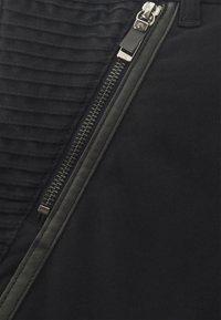 Black fabric with a textured, ribbed section and a visible zipper. Features a solid, smooth contrast material beside the zipper.