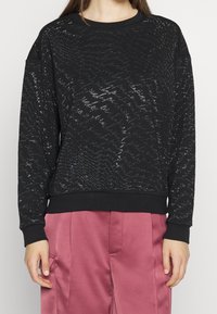 Sudadera negra con un patrón texturizado en zigzag, hecha de una tela suave. Presenta un escote redondo y puños y bajo acanalados.