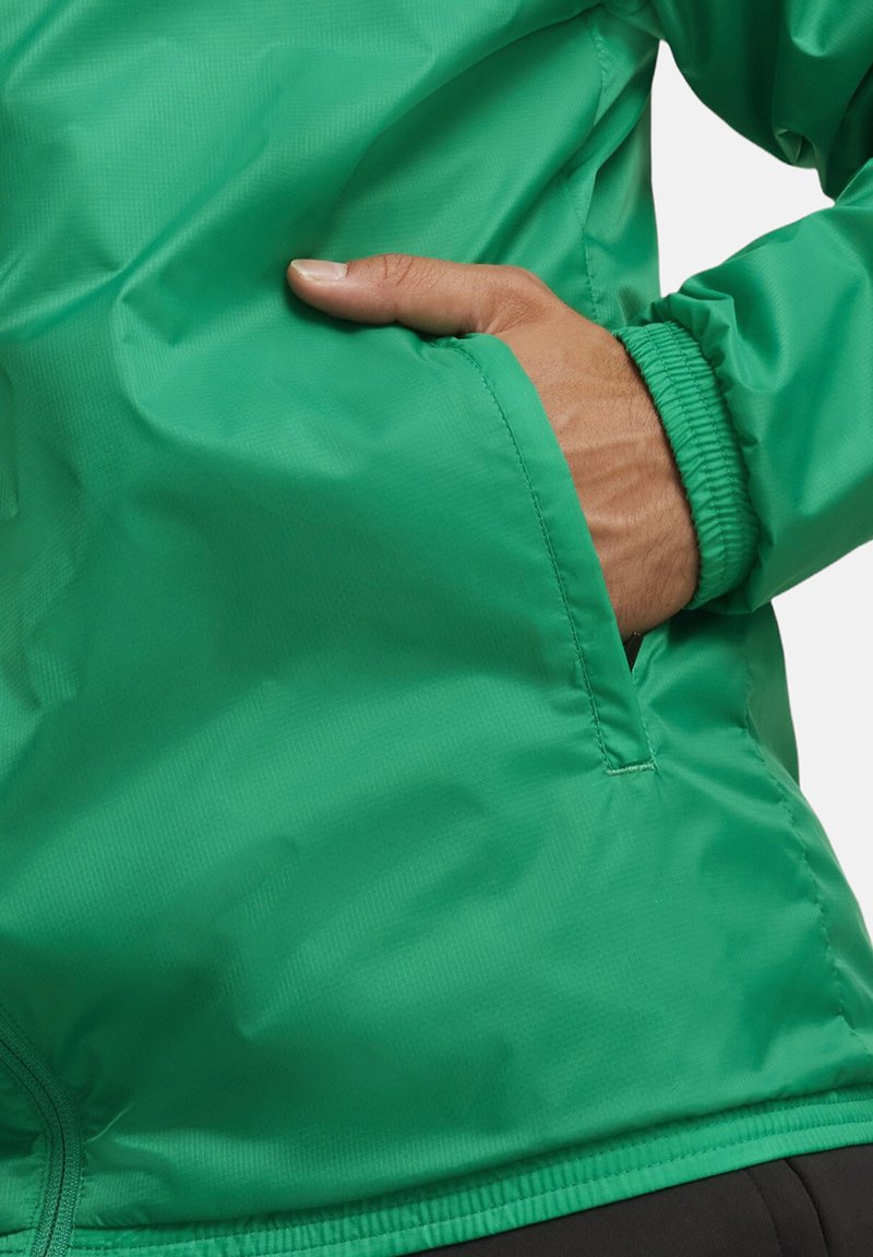 Veste en nylon verte avec une texture lisse, dotée d'un poignet élastiqué et d'une poche latérale. Coutures visibles accentuent son design élégant.