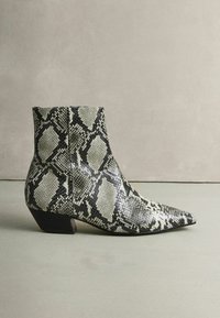 Fekete-fehér kígyóbőr mintás bokacsizma hegyes orral és alacsony tömbsarkúval. Jellemzője a texturált felület és a struktúrált sziluett.