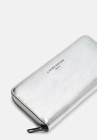 Srebrny skórzany portfel o gładkiej fakturze, z zamknięciem na zamek i wytłoczonym logo "LIEBESKIND BERLIN" z przodu.