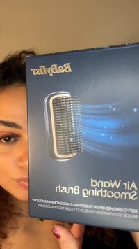 Babyliss Air Wand glattende børste i en mørkeblå eske, med metallisk kant og fine børster, med tekst som beskriver produktfordeler.