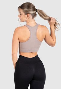Sostenedor deportivo de color marrón claro con diseño de espalda de nadador y longitud crop, combinado con leggins negros de tiro alto. Textura suave.