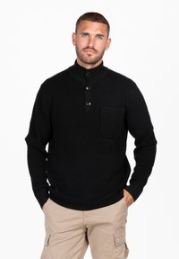Pullover nero a maglia con colletto alto, tre bottoni e tasca sul petto. Presenta polsini e orlo a coste, creando un look texture.