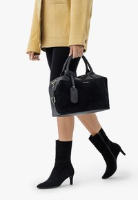 Svart mockaväska med texturerad design och handtag, ihop med svarta mocka ankelstövlar med spetsig klack och dragkedjedetalj.
