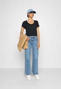 Črna majica s scoop izrezom, svetlo modra denim kapa, bež jakna, modri kavbojki širokega kroja z visokim pasom, bele športne copate, enostaven dizajn.