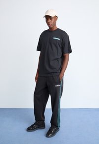 Svart bomull t-skjorte med turkise logo, kombinert med svarte treningsbukser som har tre turkise striper og hvit Adidas-merking, samt svarte joggesko.