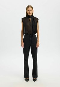 Haut noir transparent sans manches avec un détail en forme de trou de serrure, associé à un jean noir taille haute et des talons noirs à bouts pointus. Textures lisses sur l'ensemble.