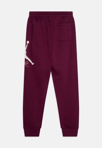 Bordowe spodnie dresowe z elastycznym pasem, zwężanymi mankietami i boczną kieszenią; posiadają biały logo Jumpman i charakterystyczny design.