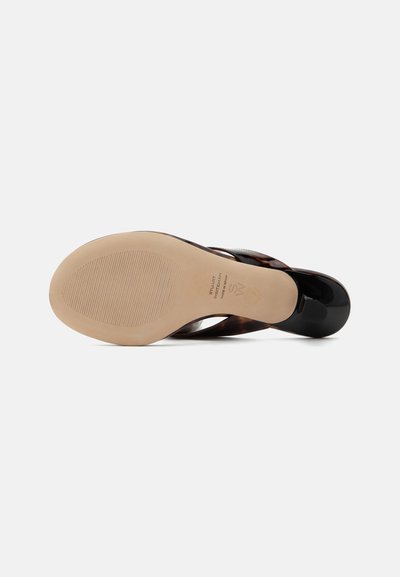 Sandale avec semelle beige texturée, bout noir verni et bride à motif écaille, vue par le dessous.