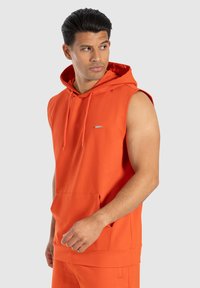 Felpa senza maniche arancione in tessuto morbido, con tasca frontale, cappuccio regolabile e un piccolo dettaglio del logo sul petto.