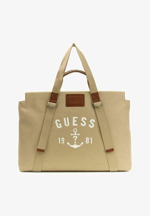 Sac fourre-tout beige Guess avec double poignée, logo ancre à l'avant et "GUESS 1981" imprimé en blanc sur le devant.