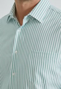 Chemise à rayures vert clair et blanche avec un col pointu, dotée d'une poche poitrine et d'un tissu texturé. Deux boutons visibles.