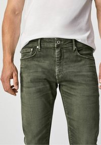 Olive green denim jeans with a slim fit, five-pocket design, and light distressing on the fabric. Metal button and rivets are present.