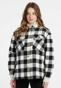 Gequilted pluchen jas in zwart en wit, met twee borstzakken, drukknoopsluiting en een relaxte pasvorm. Zachte stof met een geruit patroon.