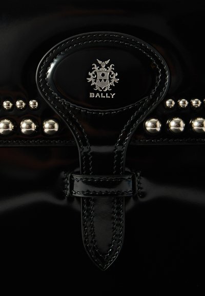 Borsa a mano in pelle nera con finitura lucida, dotata di accessori in argento, un logo prominente e borchie decorative lungo il bordo superiore.