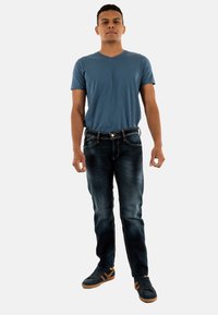 Camiseta azul de cuello en V, jeans de mezclilla oscura con áreas desgastadas y zapatillas oscuras con acentos marrones. Corte de pierna recta, estilo casual.