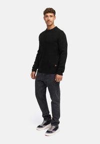 Suéter negro de punto acanalado con cuello redondo, combinado con jeans de mezclilla gris oscuro y zapatillas negras con suela blanca y detalles de cordones.