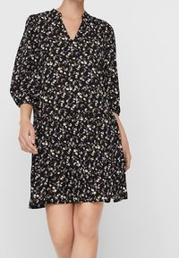 Schwarzes Blumen-Kleid mit V-Ausschnitt, Dreiviertelärmeln und gestuftem Design. Der Stoff hat kleine, bunte Blumenmuster auf der gesamten Fläche.