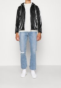 Svart blanka zip-up jacka med huva, i kombination med ljusblå slitna jeans och vita sneakers. Jackan har dragskoaccentuerade detaljer.