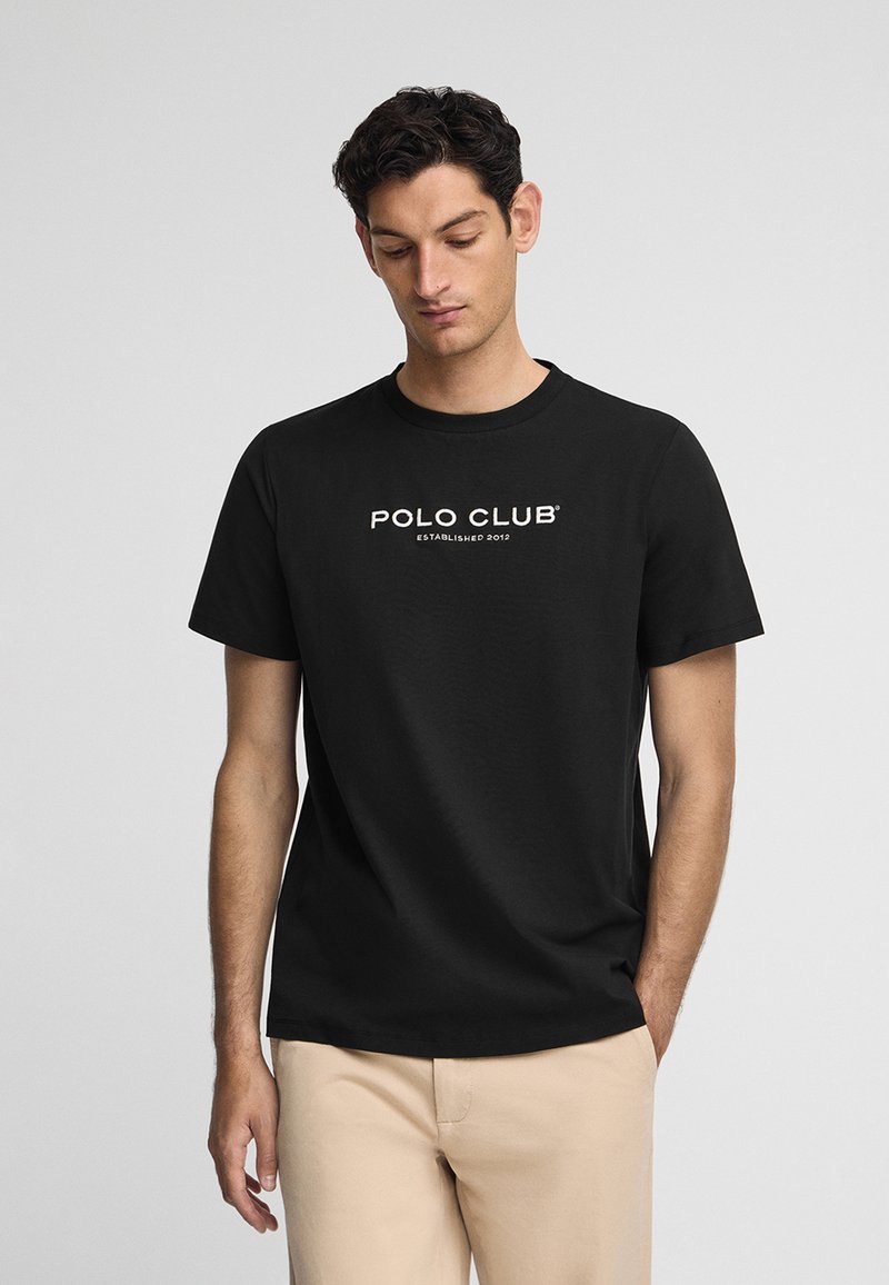 Svart bomullströja med ett vitt tryck som står "POLO CLUB" med "ETABLERAD 2012" under, rund hals, korta ärmar.