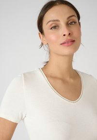 Camiseta blanca de manga corta con escote en V, con una textura suave y un diseño sencillo. Detallada con una sutileza de costura alrededor del cuello.