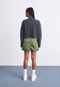 Pull cropped gris, jupe froncée vert olive, chaussettes blanches et bottes blanches chunky. Tricot texturé et tissu lisse avec des détails subtils.