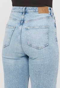 Ljusblå denimjeans med hög midja, femfickorsdesign och en läderetikett bak. Har en något urtvättad textur.