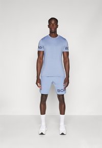 Conjunto de t-shirt e calções atléticos em azul claro. A t-shirt apresenta um logótipo nas mangas; os calções têm o logótipo na lateral. Tecido suave, design ajustado.