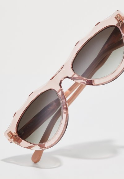 Lunettes de soleil translucides roses en forme d'œil de chat, avec des verres gris dégradés et des côtés texturés sur les montures pour plus de détail.