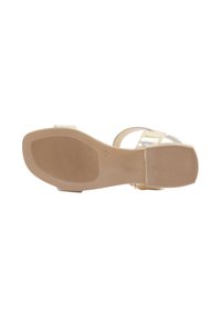Lichtbeige sandaal met metallic banden, een gestructureerde rubberen zool en een plat ontwerp met minimale details. Geschikt voor casual gebruik.
